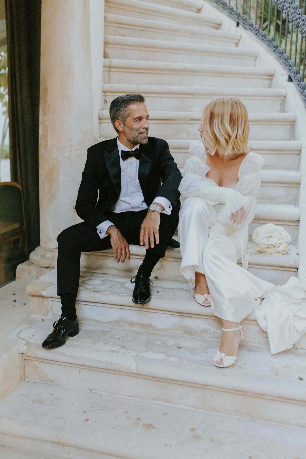 couple sitting on stairs wearing elegant outfits, highlighting civil wedding jewelry selection