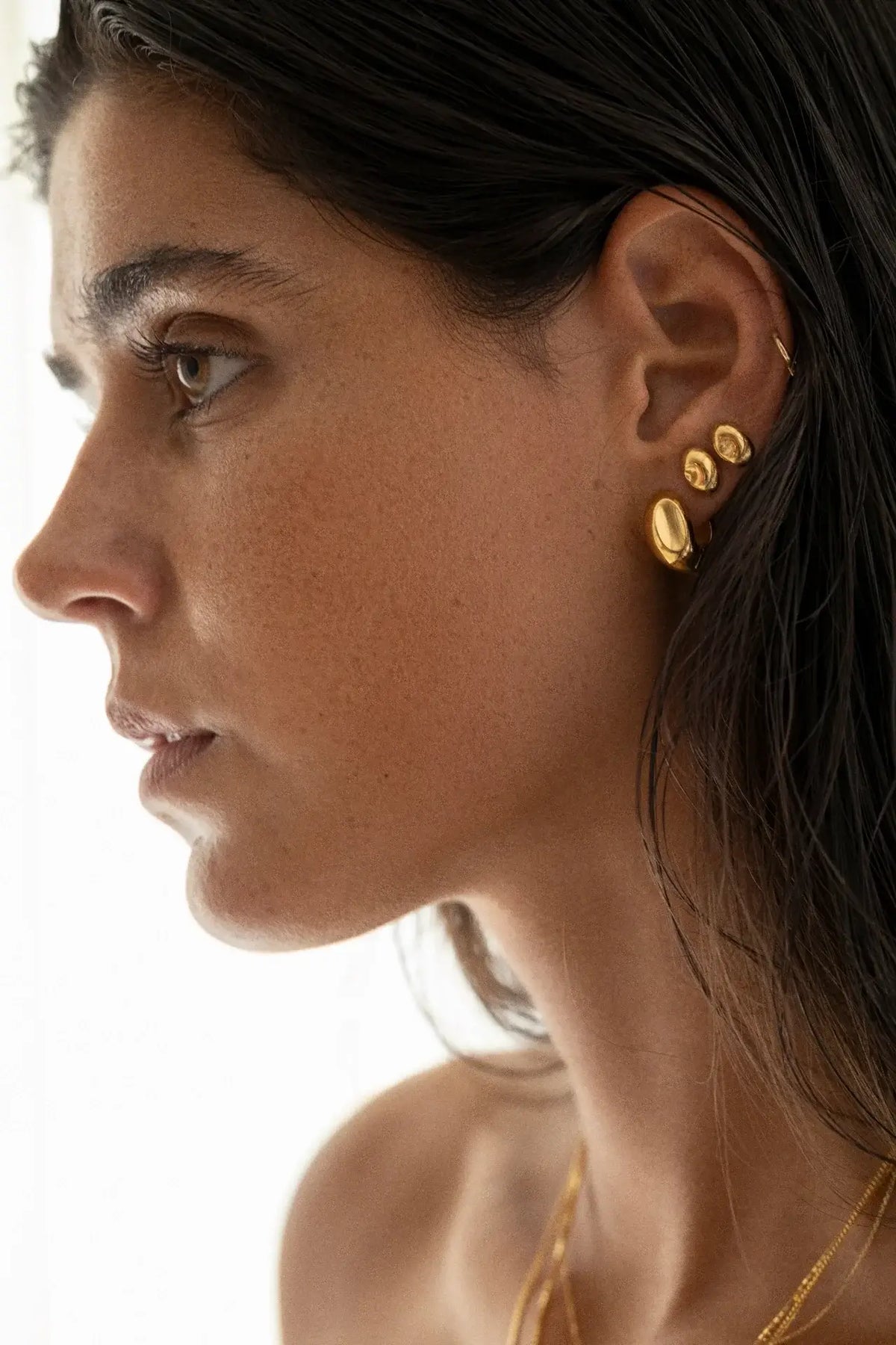 Primer plano de una mujer con pendientes de oro sobre un fondo neutro