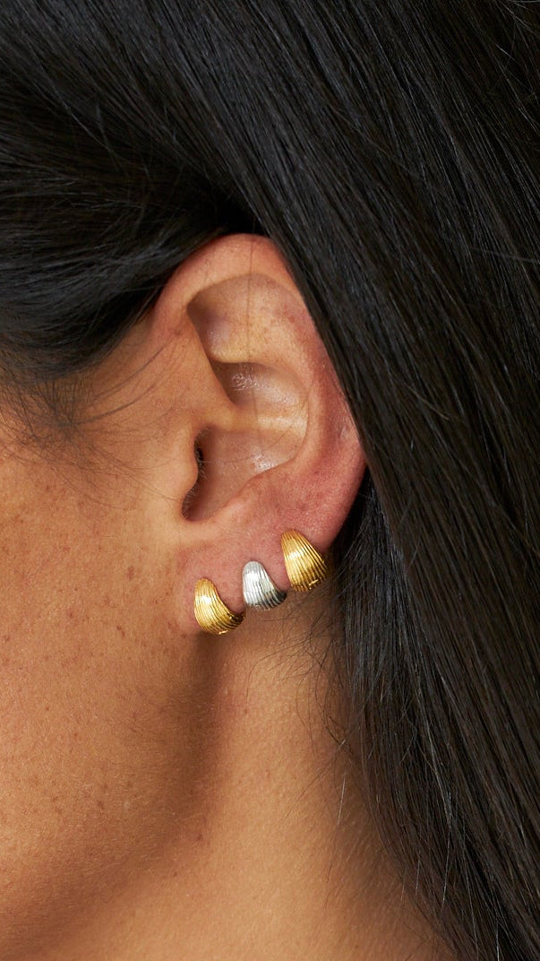 Primer plano de una oreja con pendientes de oro sobre un fondo neutro