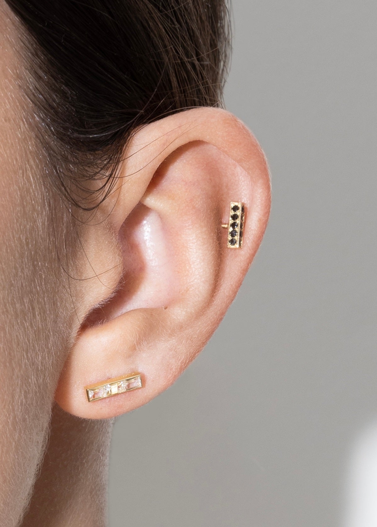 Close-up of an ear wearing gold earrings against a neutral background