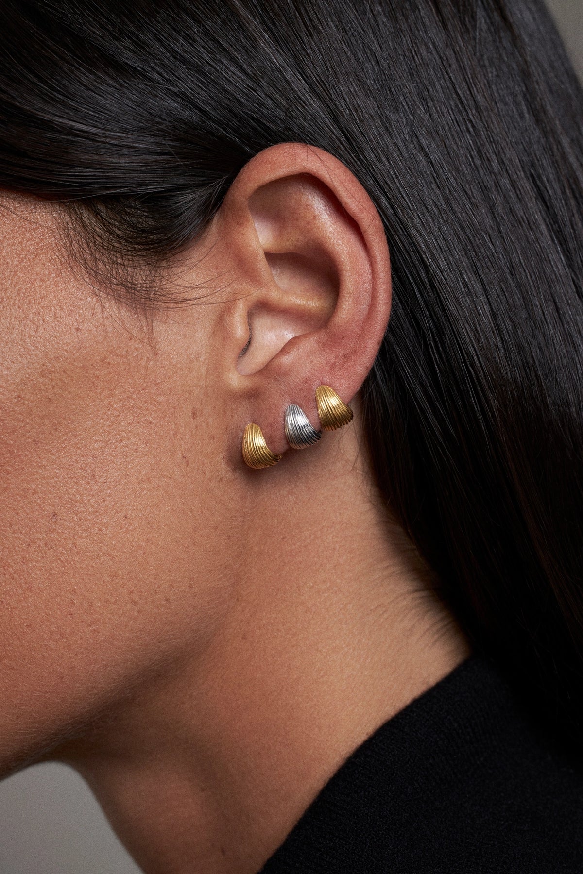 Tilly Huggie Earrings comfortable everyday wear present worn in a model's ear, showcasing silver and gold finishes.