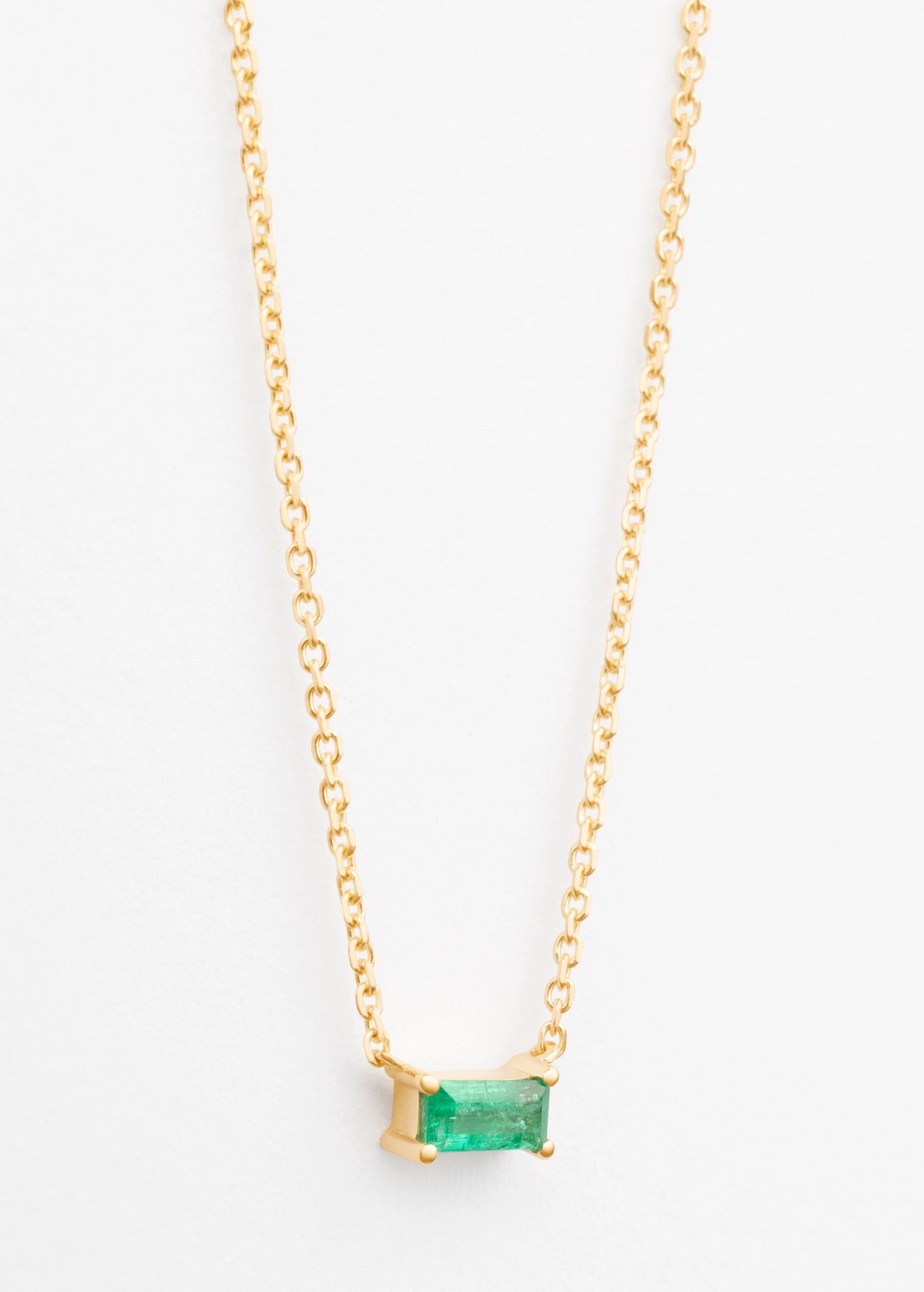 Gold necklace with a green gemstone on a white background