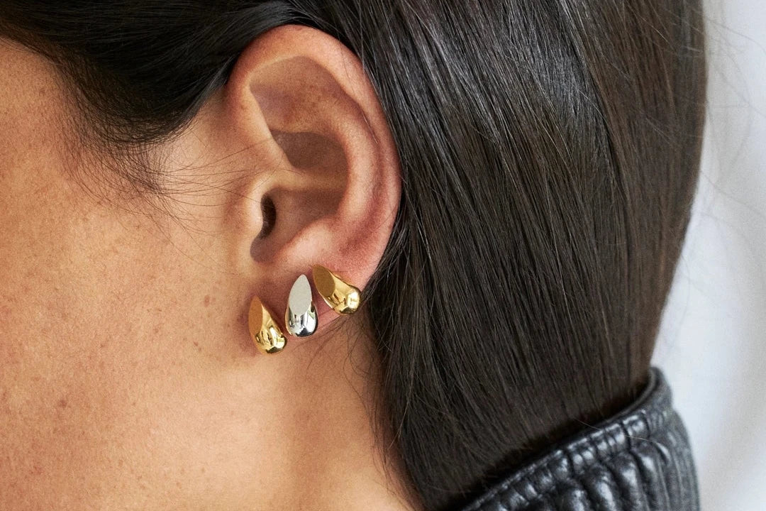 Close-up of a person wearing gold earrings with a black ribbed sweater.