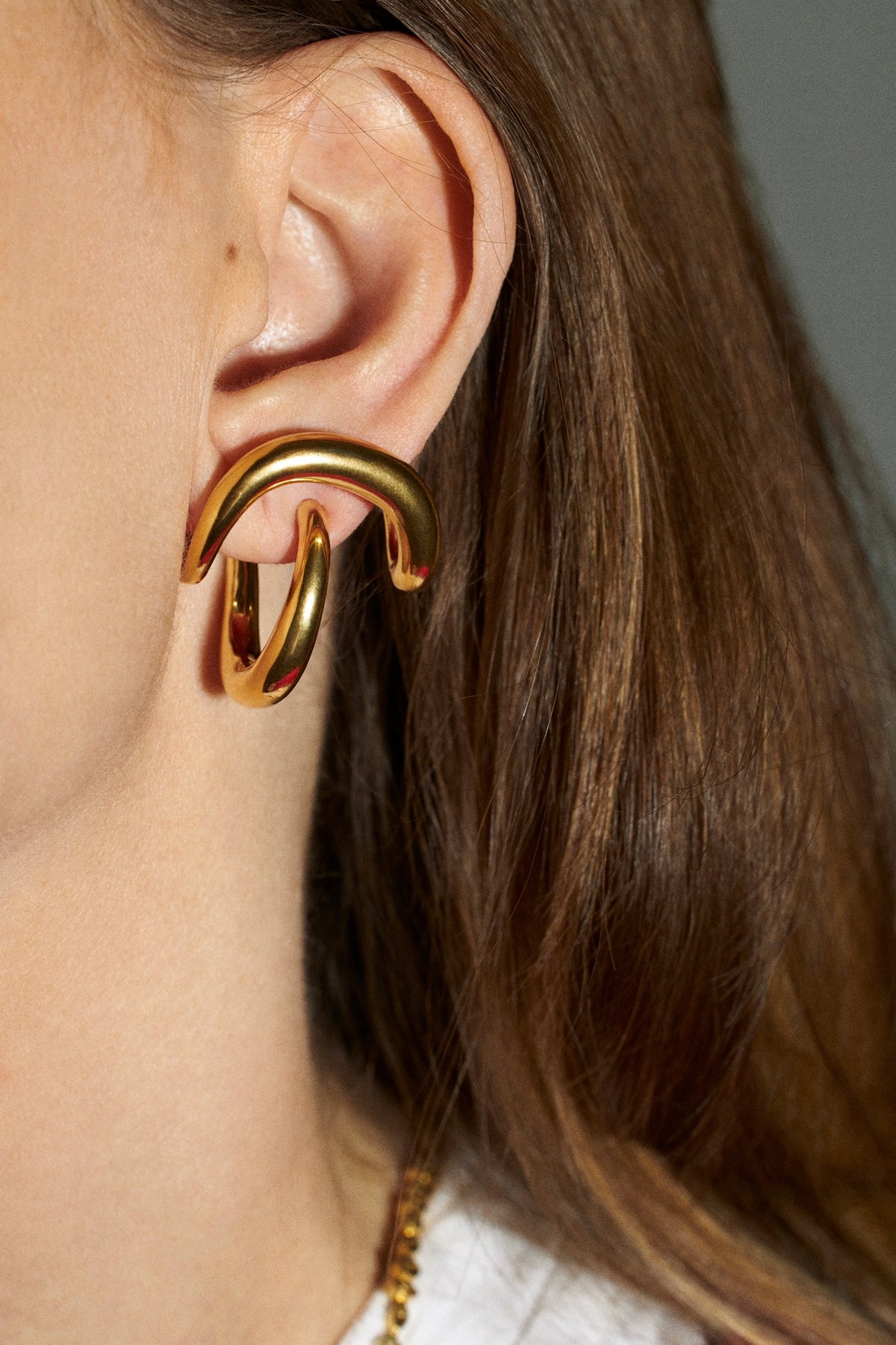 A close-up of a model's ear wearing a chunky, multi-layered gold hoop earring.