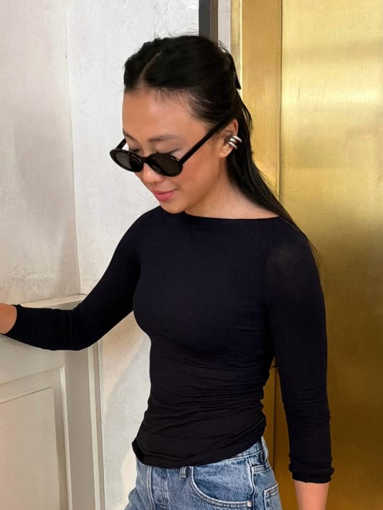 Judy Kam wearing a black long-sleeve top and blue jeans, standing against a gold wall with charli ear cuff from cinco in silver