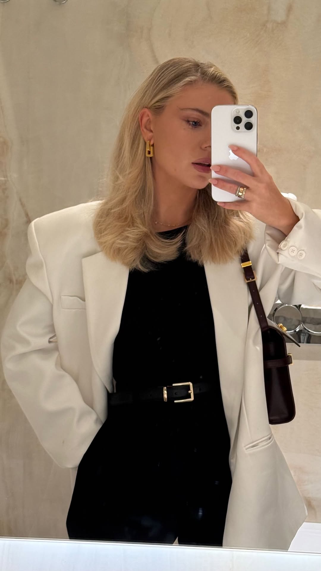 CINCO jewelry model wearing gold earrings with a white blazer in a mirror reflection.