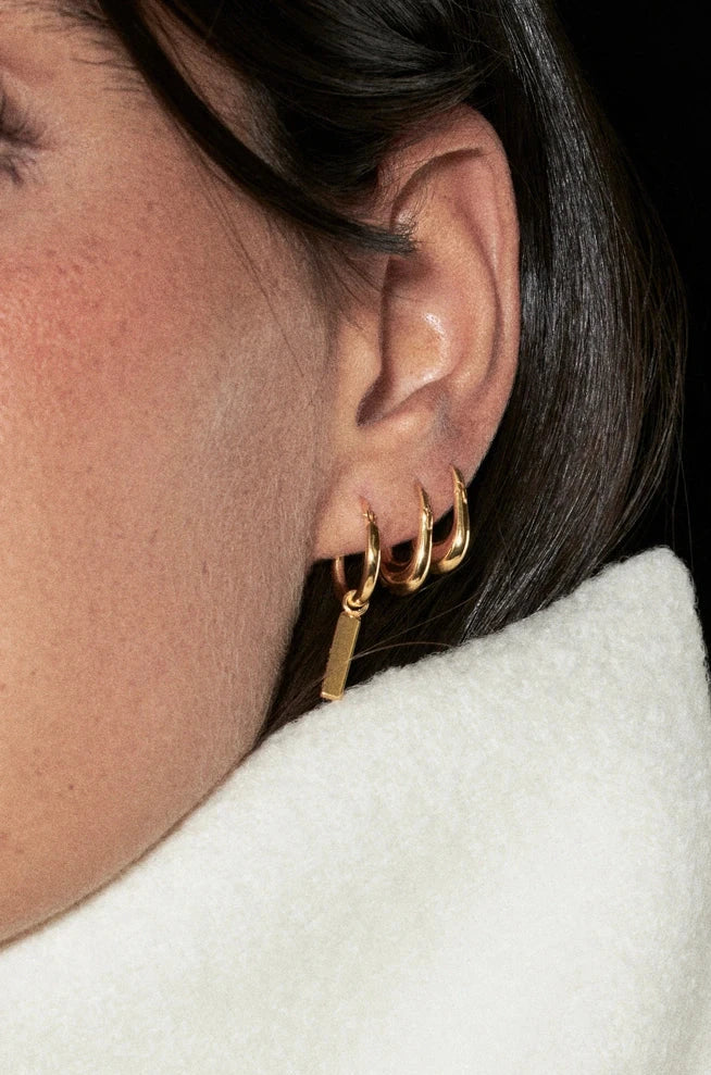 Close-up of a person wearing gold hoop earrings with a white garment and dark background