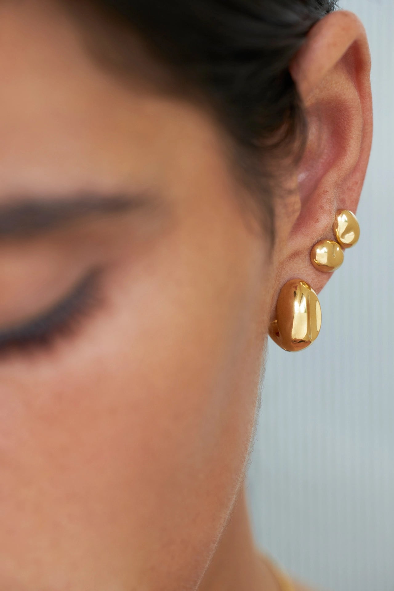 Primer plano de una persona usando pendientes de oro con un fondo neutro