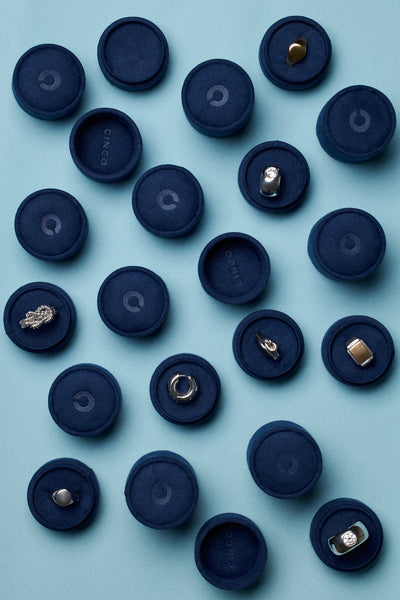 Arrangement of tiny velvet jewelry boxes with various jewelry pieces on a soft blue background.